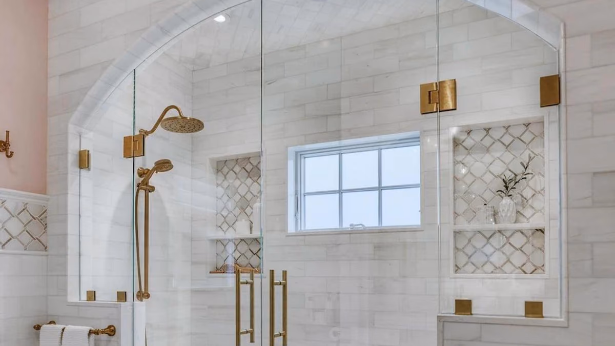Marble walk-in shower with an arched glass enclosure, brushed-gold fixtures, tiled niches, and a mosaic floor