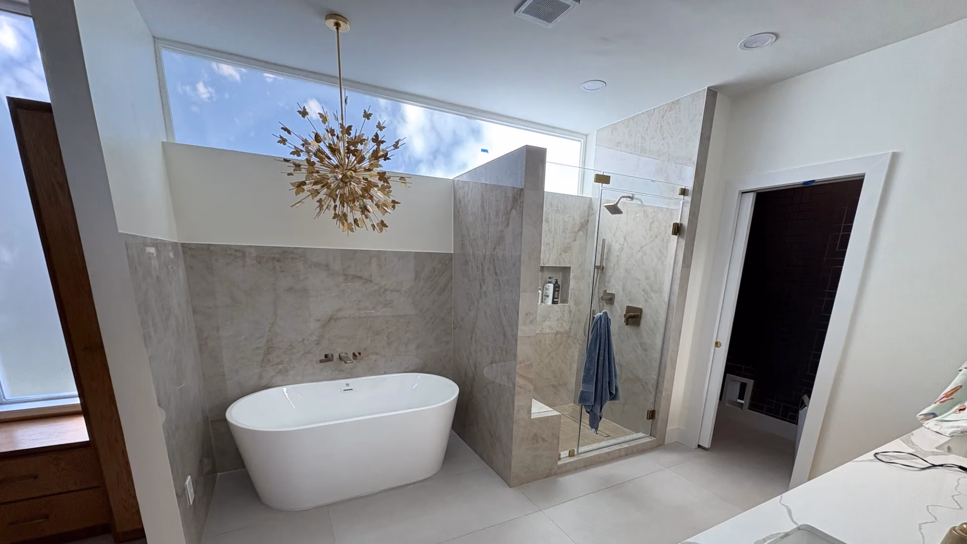 Completed primary bathroom with a freestanding soaking tub, a glass-enclosed walk-in shower, large-format marble-look tile, and a starburst chandelier