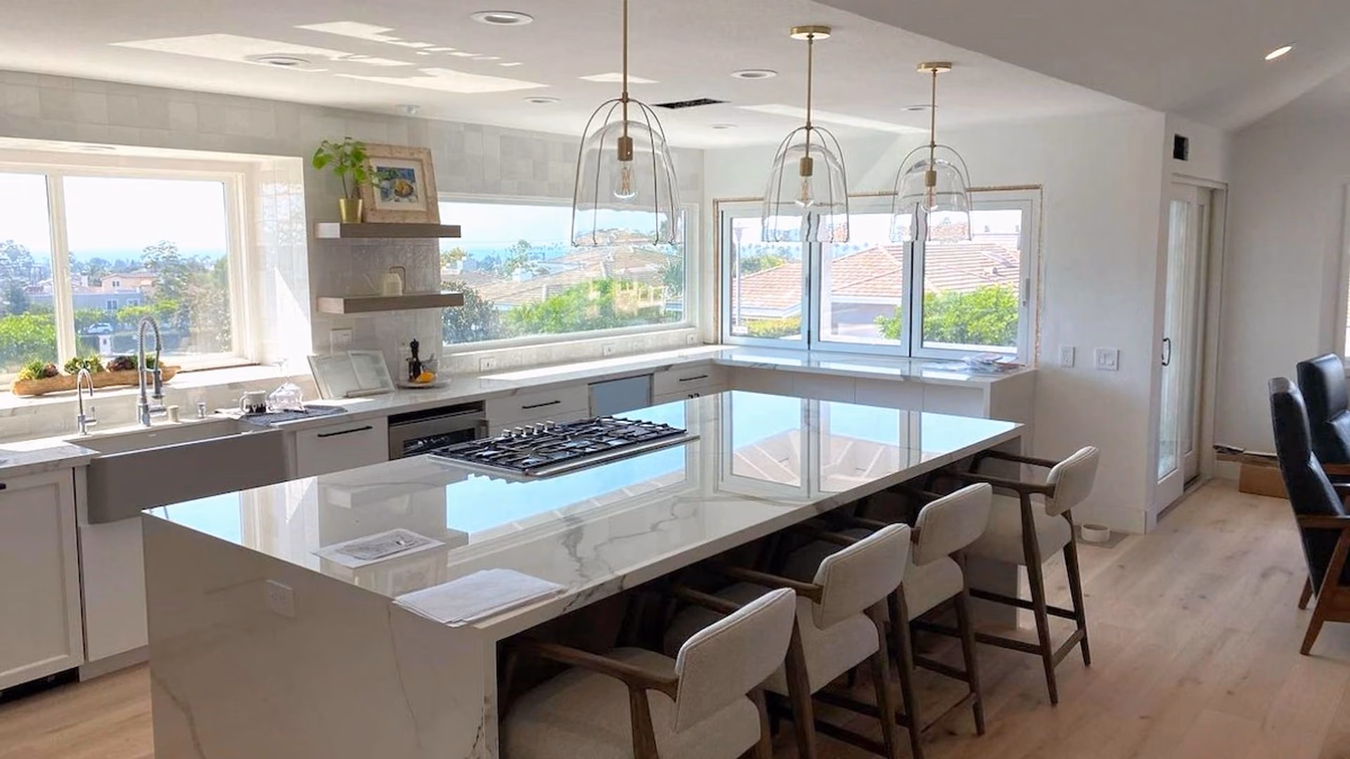 Open-plan living and kitchen area after renovation, with a large quartz island, bar seating, pendant lights, a gas cooktop, and a wall of view windows
