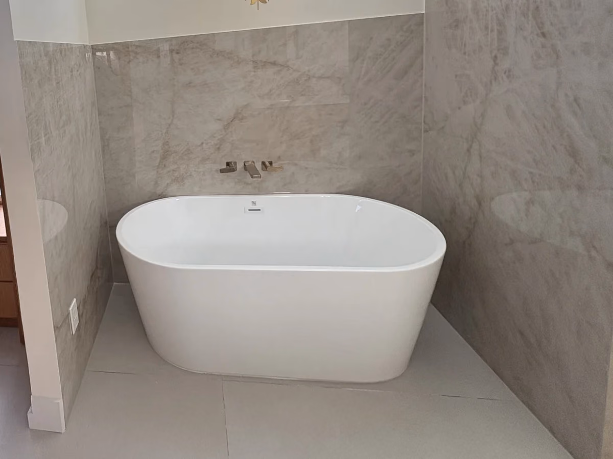 Freestanding soaking tub with a wall-mounted filler against full-height marble-look tile in a remodeled primary bathroom