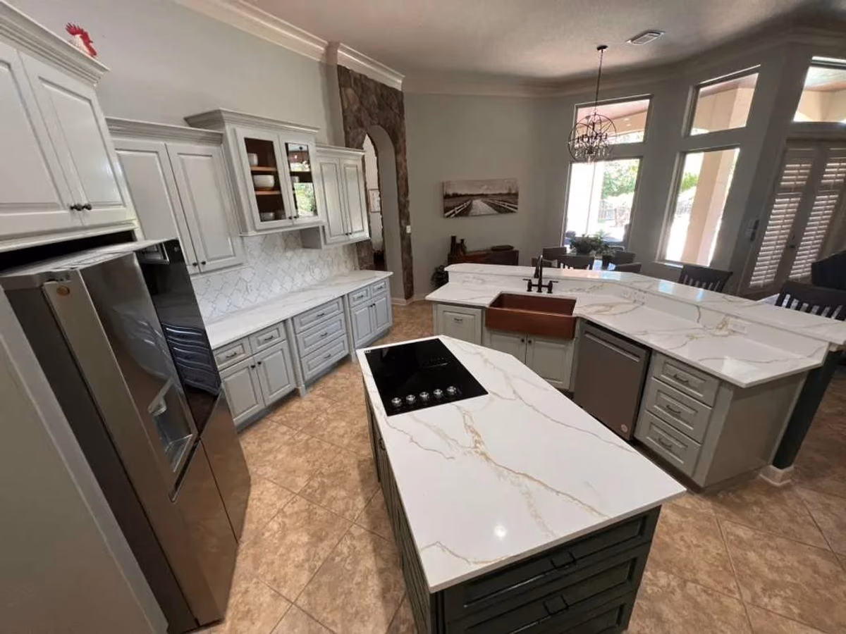 Kitchen with a sage-green cooktop island, white quartz countertops with gold veining, gray perimeter cabinets, stainless appliances, and an arched opening to the adjoining room