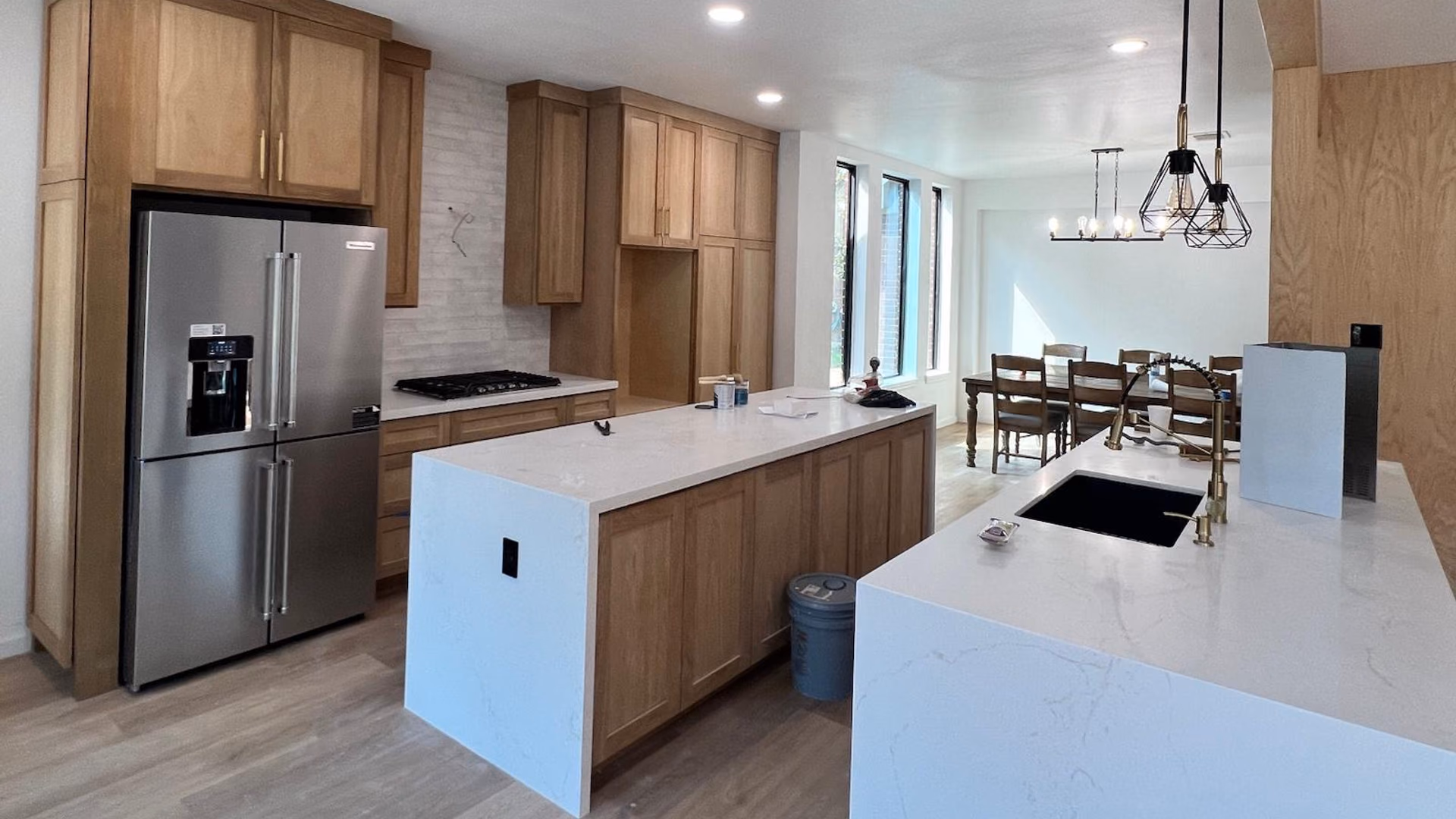 Open-plan remodel with a wood-cabinet kitchen, a white quartz waterfall island, and an adjoining dining area under a linear chandelier
